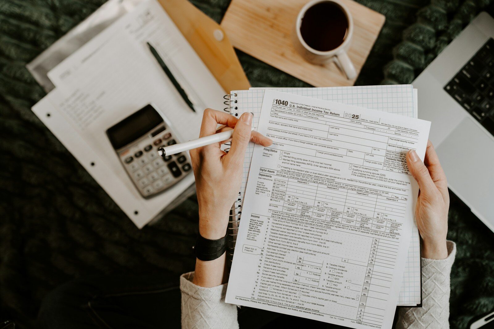 Person reviewing documents with calculator and laptop.